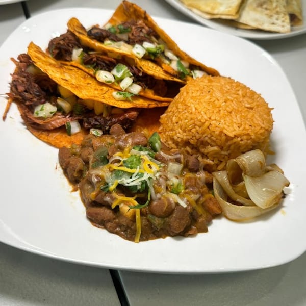 Three halal tacos with rice, beans, and grilled onions on a white plate.