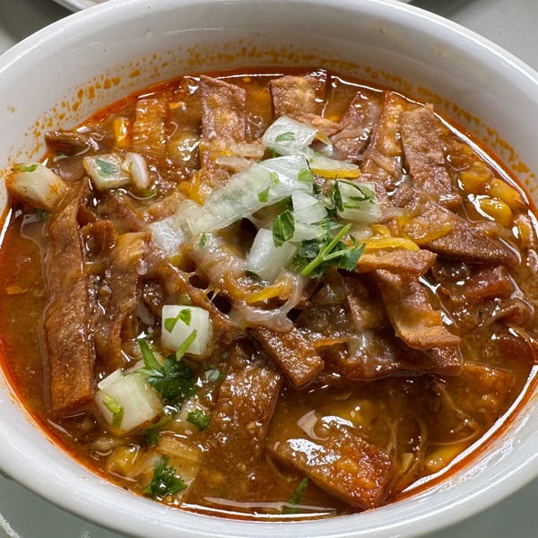 Halal Cuts' birria ramen, a rich red broth with noodles, meat, onions, cilantro, and melted cheese.
