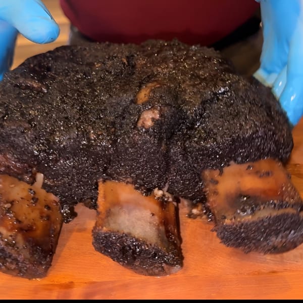 A chef in blue gloves carves a large, dark, smoked halal brisket on a wooden board.