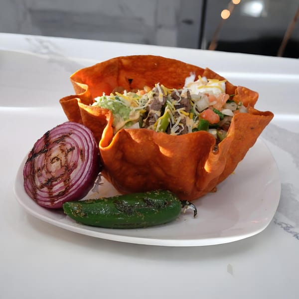 Halal Cuts taco salad in an edible bowl with grilled onion and jalapeño on a white plate.