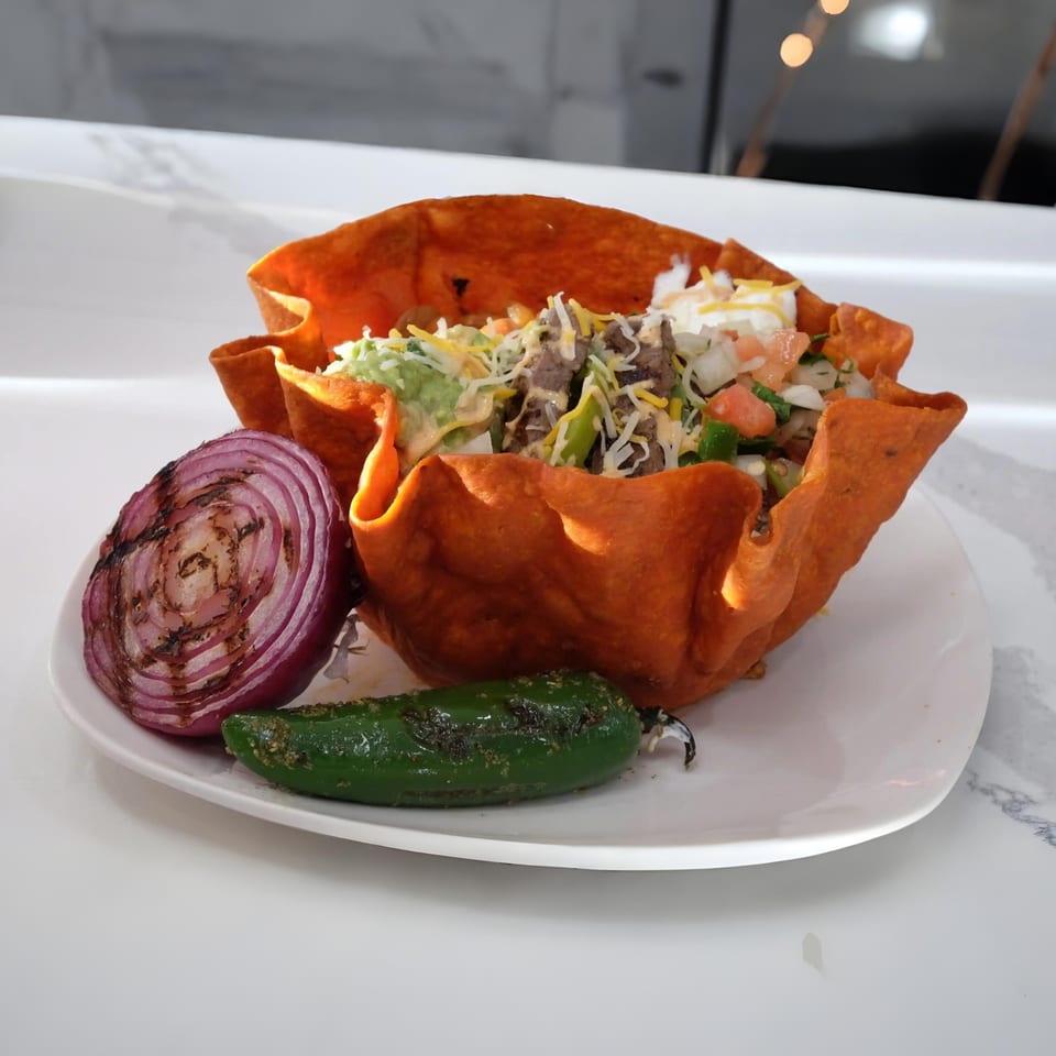 Halal Cuts taco salad in an edible bowl with grilled onion and jalapeño on a white plate.