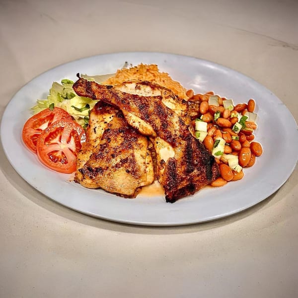 Halal Cuts' grilled chicken with rice, beans, lettuce, and sliced tomatoes on a white plate.